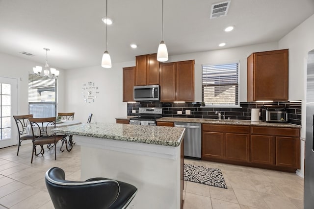 kitchen with appliances with stainless steel finishes, tasteful backsplash, hanging light fixtures, sink, and light tile patterned flooring