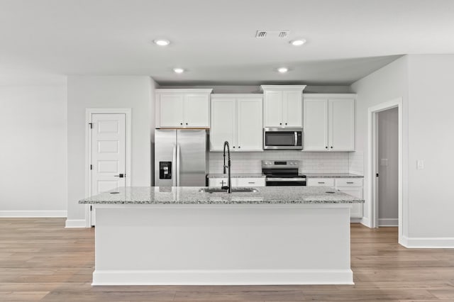 kitchen with stainless steel appliances, light stone countertops, sink, and a center island with sink