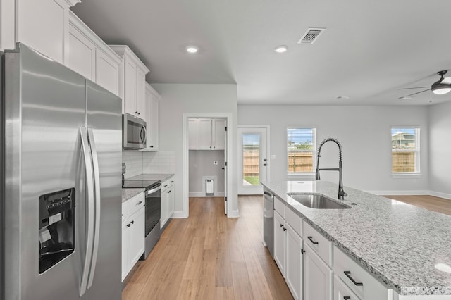 kitchen with tasteful backsplash, an island with sink, sink, white cabinets, and stainless steel appliances