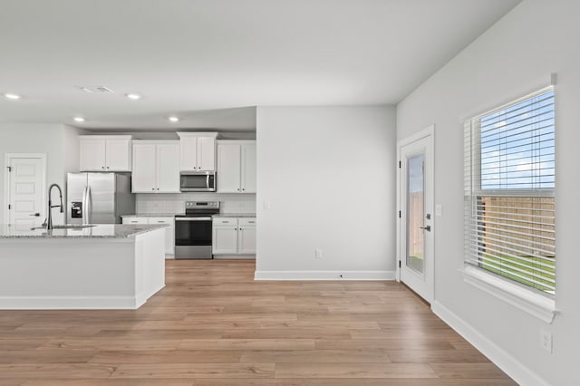 kitchen with stainless steel appliances, light stone counters, light hardwood / wood-style floors, white cabinets, and decorative backsplash