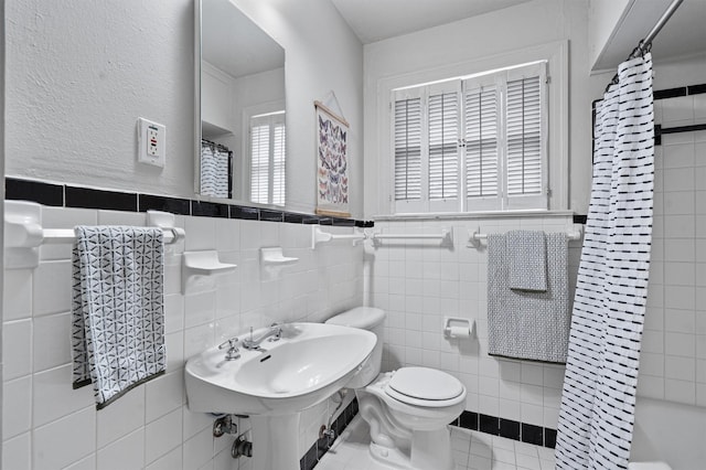 full bathroom featuring toilet, a healthy amount of sunlight, and tile walls