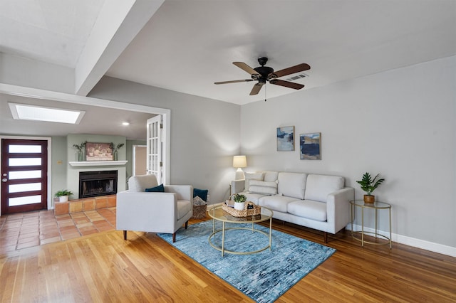 living room with hardwood / wood-style flooring, a skylight, ceiling fan, and a fireplace