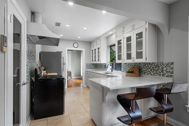 kitchen featuring white cabinets, kitchen peninsula, stainless steel refrigerator, and a kitchen bar