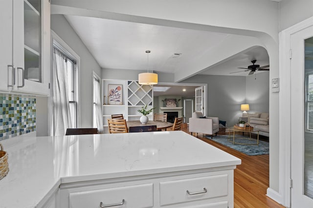 kitchen featuring ceiling fan, white cabinetry, light wood-type flooring, pendant lighting, and backsplash