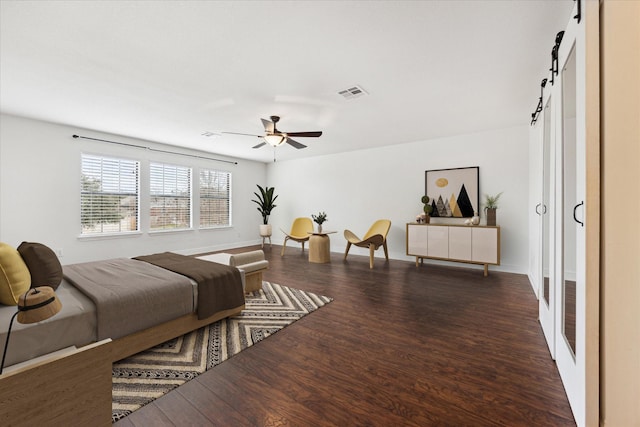 bedroom featuring ceiling fan, dark hardwood / wood-style flooring, and a barn door