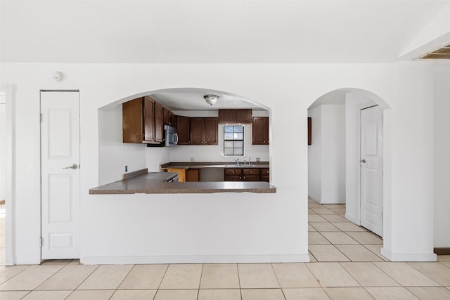 kitchen featuring sink, dark brown cabinetry, kitchen peninsula, and light tile patterned floors