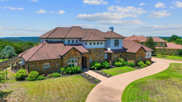 mediterranean / spanish home featuring fence, a tile roof, stone siding, a front yard, and a chimney