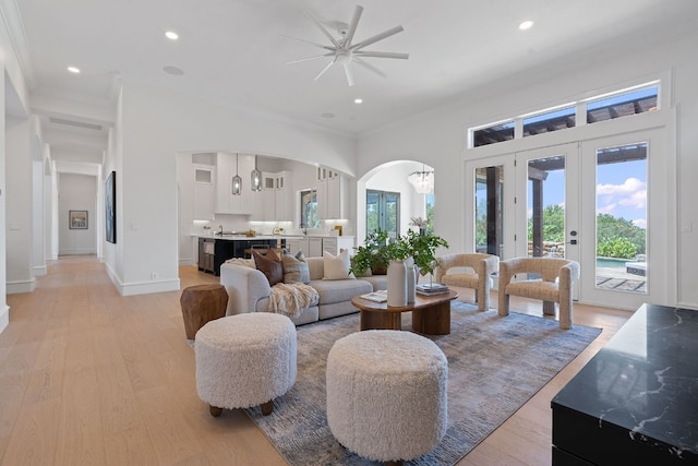 living room featuring crown molding, arched walkways, ceiling fan, and light wood-style floors