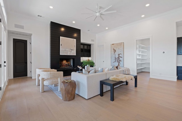 living room with built in shelves, ornamental molding, light hardwood / wood-style flooring, and a large fireplace