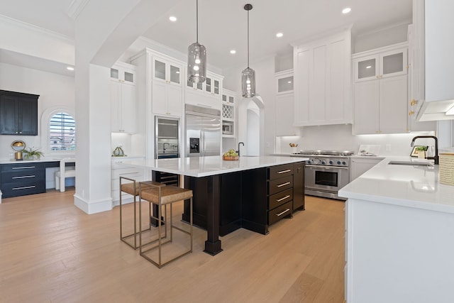 kitchen with premium appliances, hanging light fixtures, sink, white cabinets, and a center island