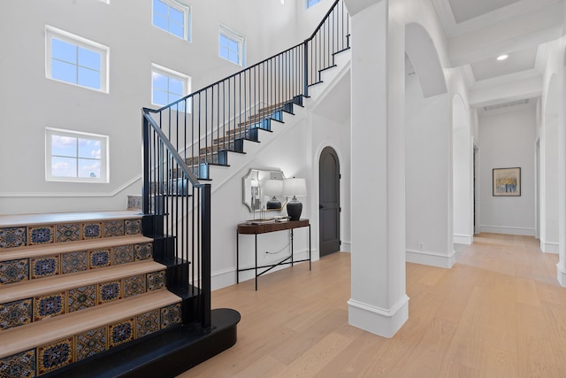 stairs with a towering ceiling, ornamental molding, and wood-type flooring