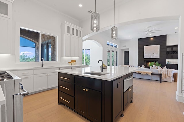 kitchen with sink, decorative light fixtures, white cabinetry, and a kitchen island with sink