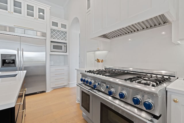 kitchen with built in appliances, crown molding, white cabinetry, light hardwood / wood-style flooring, and wall chimney exhaust hood