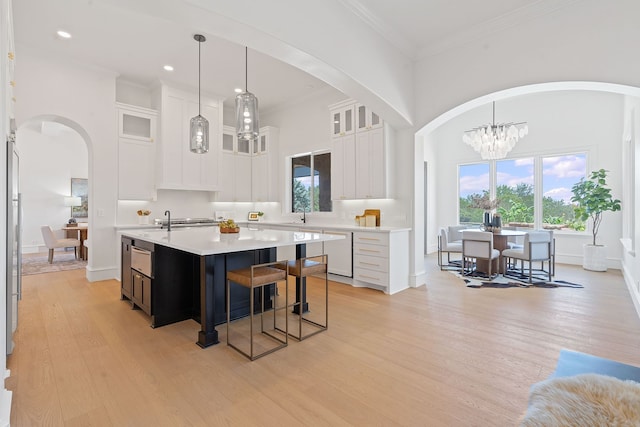 kitchen featuring decorative light fixtures, white cabinetry, white dishwasher, and an island with sink