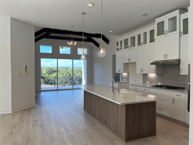 kitchen featuring decorative light fixtures, white cabinetry, an island with sink, stainless steel gas stovetop, and beam ceiling