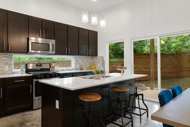 kitchen with sink, a kitchen island with sink, appliances with stainless steel finishes, and a kitchen breakfast bar