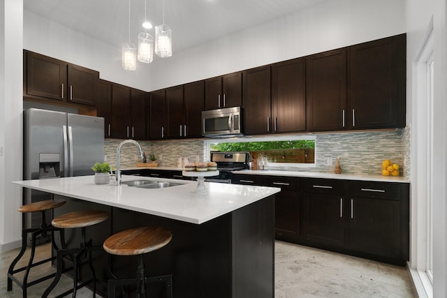 kitchen with appliances with stainless steel finishes, a kitchen bar, an island with sink, sink, and dark brown cabinets