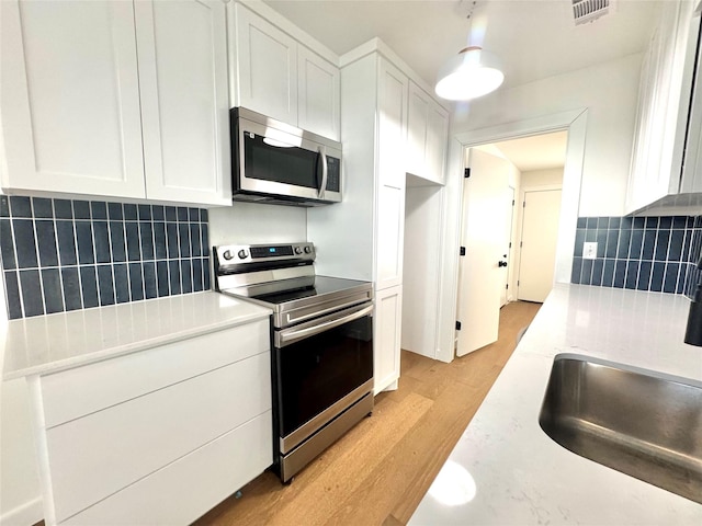 kitchen with backsplash, white cabinetry, appliances with stainless steel finishes, and light wood-type flooring