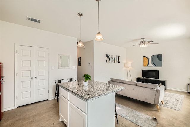 kitchen with a kitchen bar, white cabinets, decorative light fixtures, a kitchen island, and light stone counters