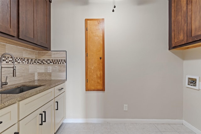 kitchen with tasteful backsplash, light tile patterned floors, sink, cream cabinetry, and light stone counters