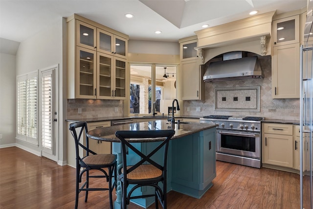 kitchen featuring wall chimney exhaust hood, dark wood-type flooring, stainless steel range, a breakfast bar, and a center island with sink