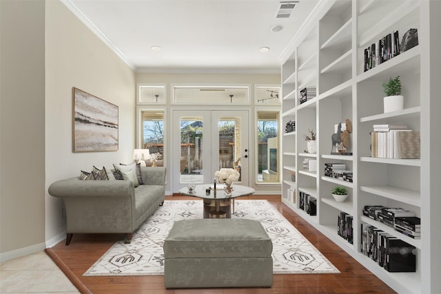 living area with built in shelves, light hardwood / wood-style flooring, crown molding, and french doors