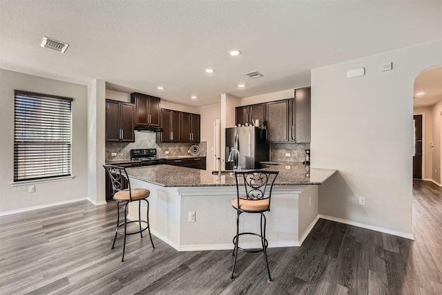 kitchen with a kitchen breakfast bar, dark brown cabinets, kitchen peninsula, stainless steel fridge with ice dispenser, and dark stone countertops