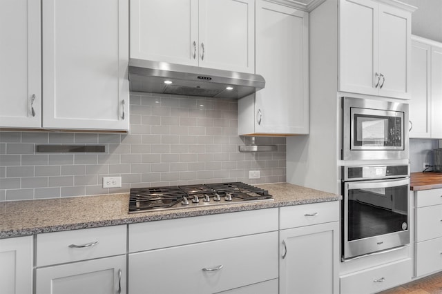 kitchen with white cabinets, tasteful backsplash, light stone countertops, and appliances with stainless steel finishes