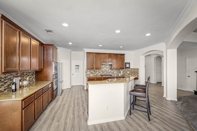 kitchen with light wood-type flooring, stainless steel appliances, light stone counters, and crown molding