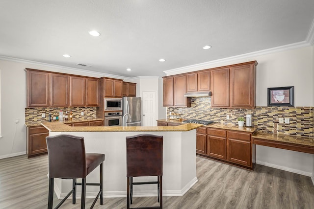 kitchen featuring a kitchen bar, stainless steel appliances, light hardwood / wood-style floors, a center island with sink, and crown molding