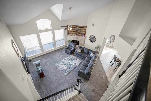 carpeted living room featuring a towering ceiling, a stone fireplace, and ceiling fan