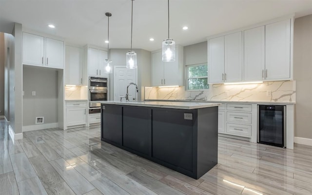2718 Leslie Ln, San Marcos, TX 78666 - kitchen with beverage cooler, white cabinets, double oven, an island with sink, and recessed lighting