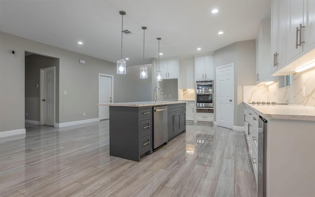 kitchen with white cabinets, stainless steel appliances, tasteful backsplash, and an island with sink