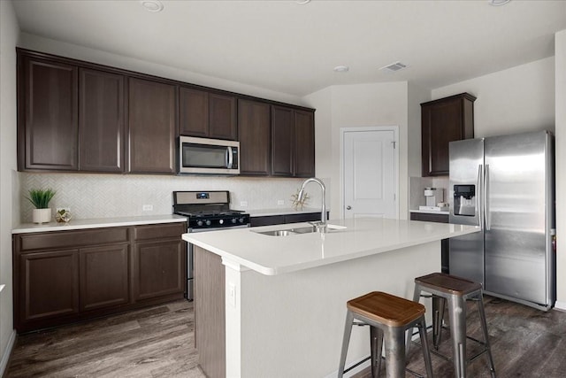 kitchen featuring dark brown cabinetry, dark wood-type flooring, stainless steel appliances, an island with sink, and sink