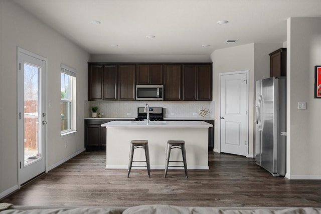 kitchen featuring a kitchen bar, sink, dark hardwood / wood-style flooring, stainless steel appliances, and a center island with sink