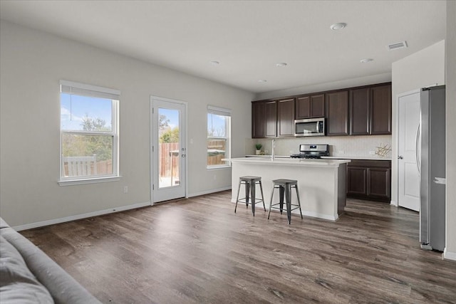 kitchen with plenty of natural light, a kitchen island with sink, a breakfast bar, stainless steel appliances, and dark hardwood / wood-style floors