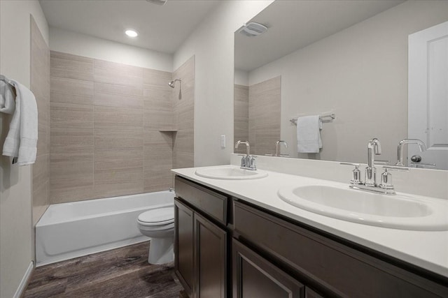 full bathroom featuring vanity, hardwood / wood-style flooring, tiled shower / bath combo, and toilet