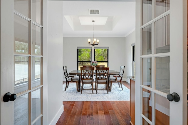 dining area with wood-type flooring, french doors, a tray ceiling, ornamental molding, and an inviting chandelier