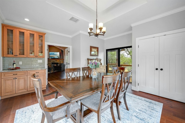 dining space featuring crown molding, an inviting chandelier, dark hardwood / wood-style floors, and a stone fireplace