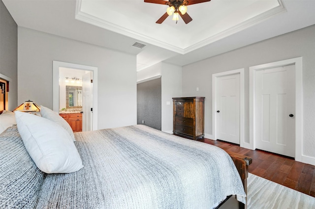 bedroom featuring ceiling fan, dark hardwood / wood-style flooring, a tray ceiling, ornamental molding, and connected bathroom