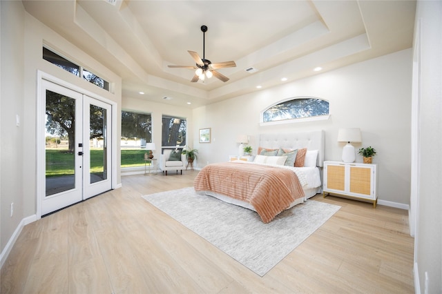 bedroom with french doors, light hardwood / wood-style floors, access to outside, a raised ceiling, and ceiling fan