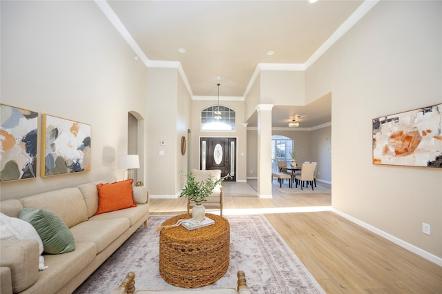 living room with a towering ceiling, ornamental molding, and light hardwood / wood-style floors