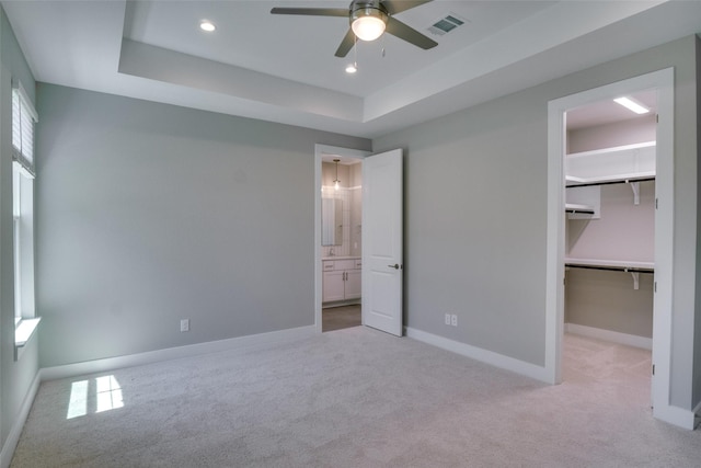 unfurnished bedroom featuring ceiling fan, a closet, a walk in closet, and a raised ceiling