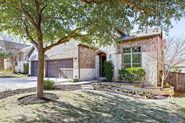 view of front of home featuring driveway, a garage, stone siding, fence, and brick siding