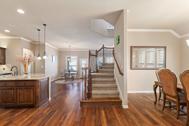 kitchen with dark wood-type flooring, ornamental molding, light stone countertops, and hanging light fixtures