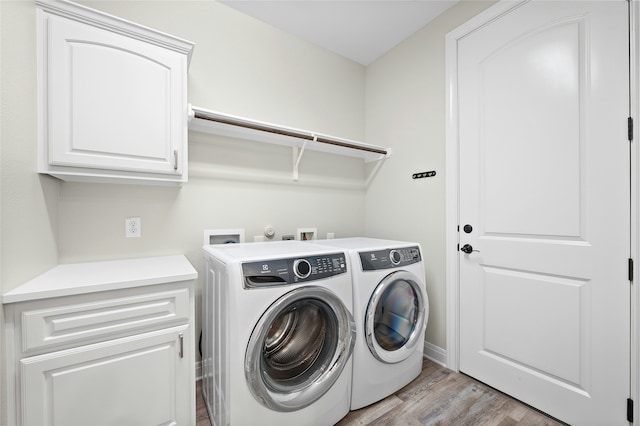 laundry room with light wood-type flooring, washing machine and clothes dryer, and cabinets