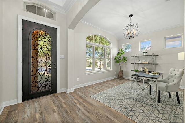 entrance foyer featuring hardwood / wood-style flooring, a chandelier, ornamental molding, and lofted ceiling