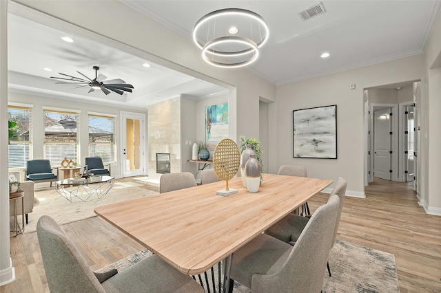 dining room featuring ornamental molding, light hardwood / wood-style floors, a tray ceiling, and a large fireplace