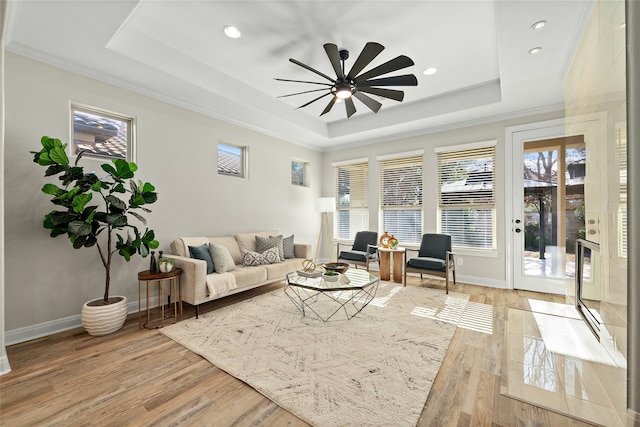 living room with ceiling fan, a tray ceiling, ornamental molding, and light wood-type flooring