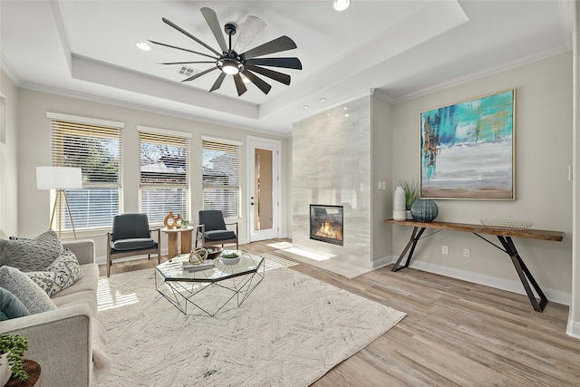 living room with a premium fireplace, ceiling fan, a raised ceiling, and crown molding